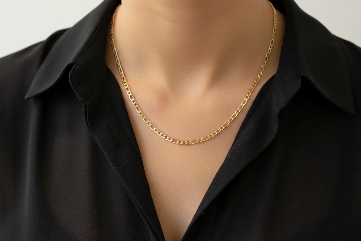 Close-up of a person wearing a 14K gold-filled Figaro chain necklace over a white shirt.